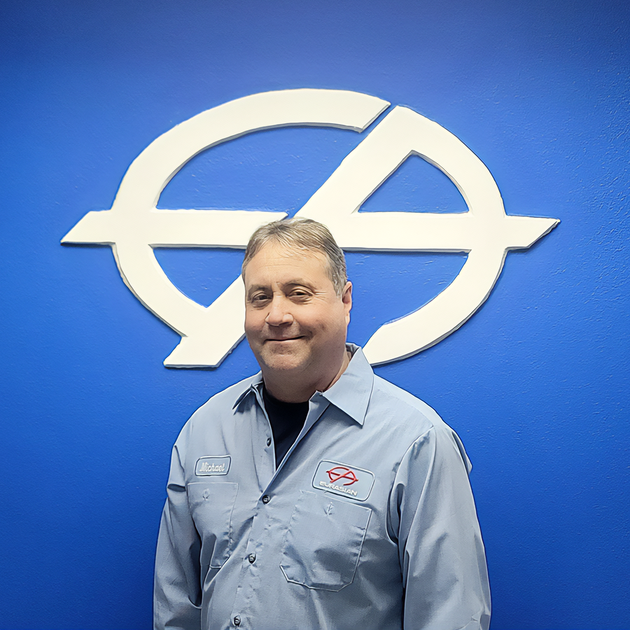 Man in blue shirt smiles in front of a blue wall with a white logo.