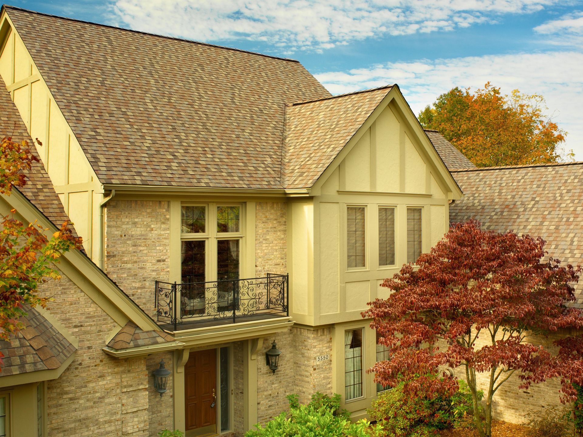 A large brick house with a balcony and a tree in front of it