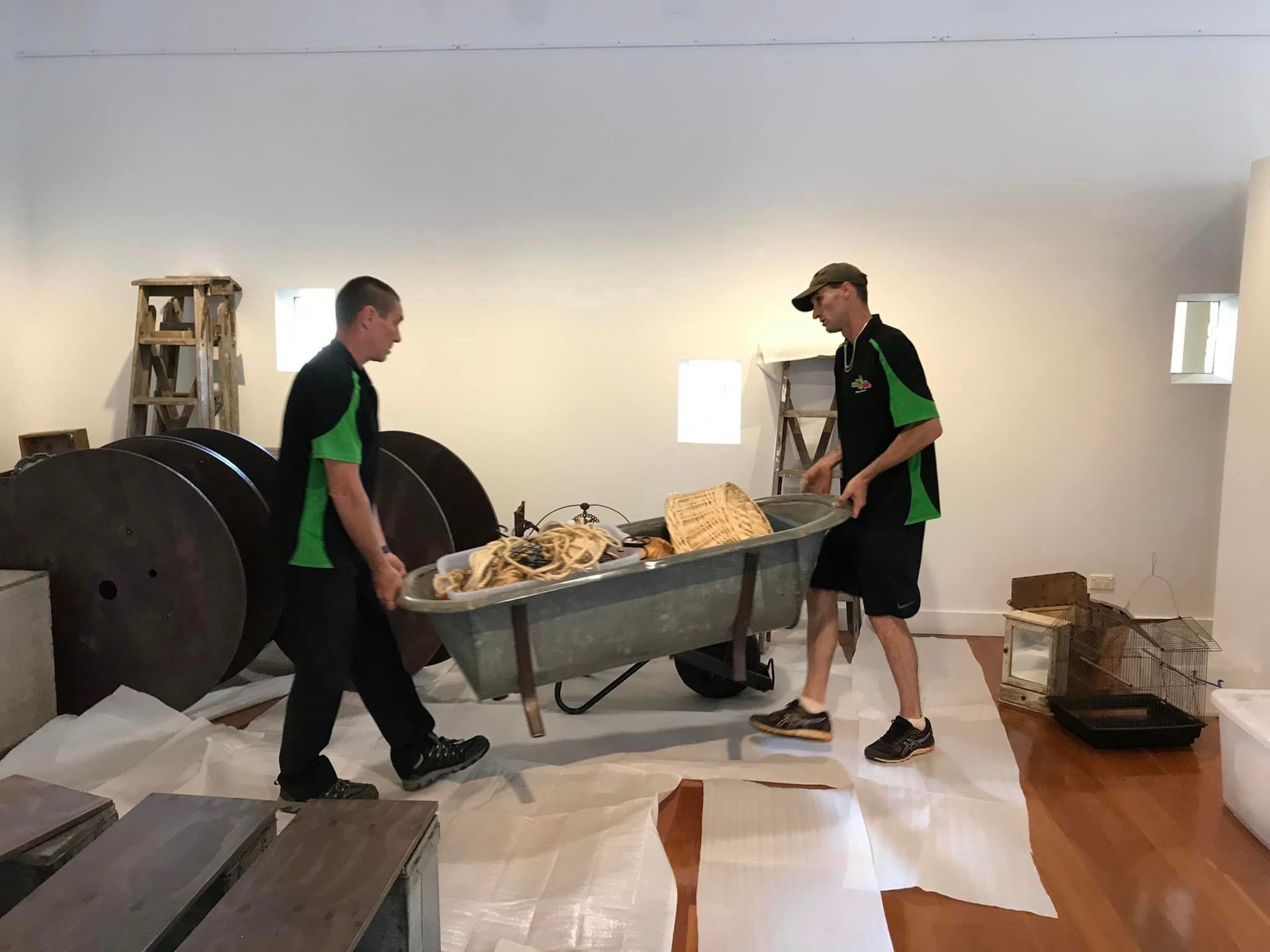 Two Movers Carrying a Loaded Wheelbarrow Across a Room — Little Green Truck Bundaberg In Bargara, QLD