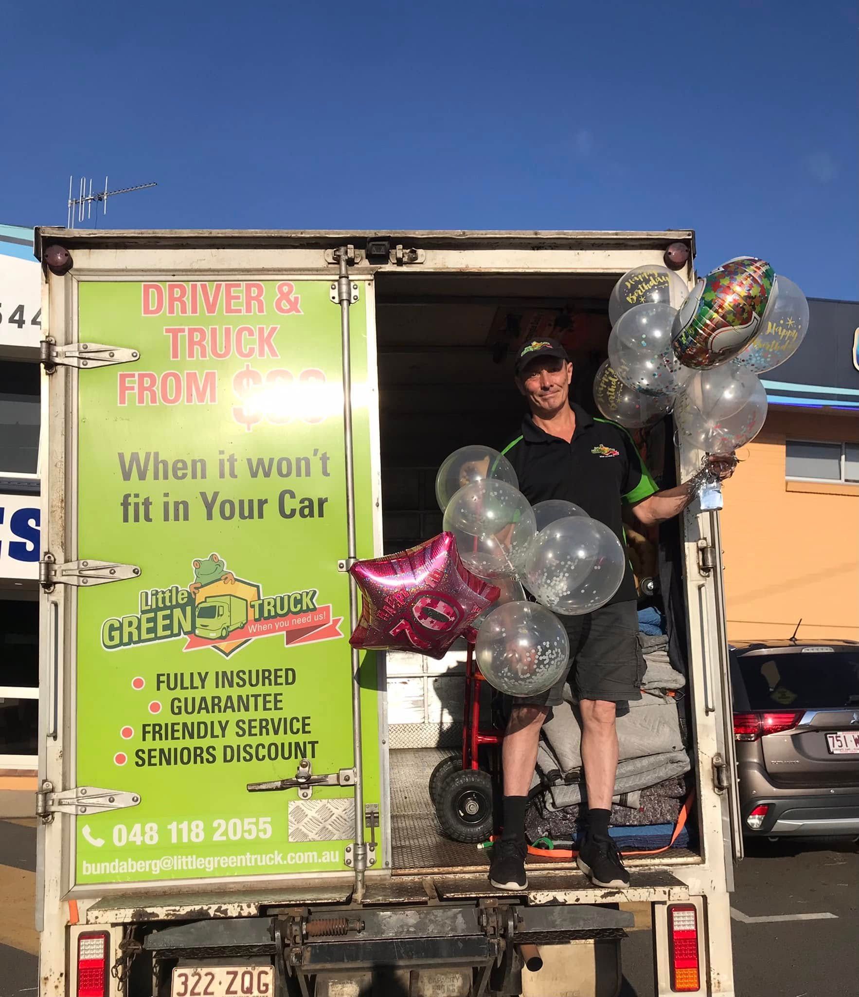 Man Standing in a Truck With Signs for Delivery Services, Surrounded by Balloons — Little Green Truck Bundaberg In Woodgate, QLD
