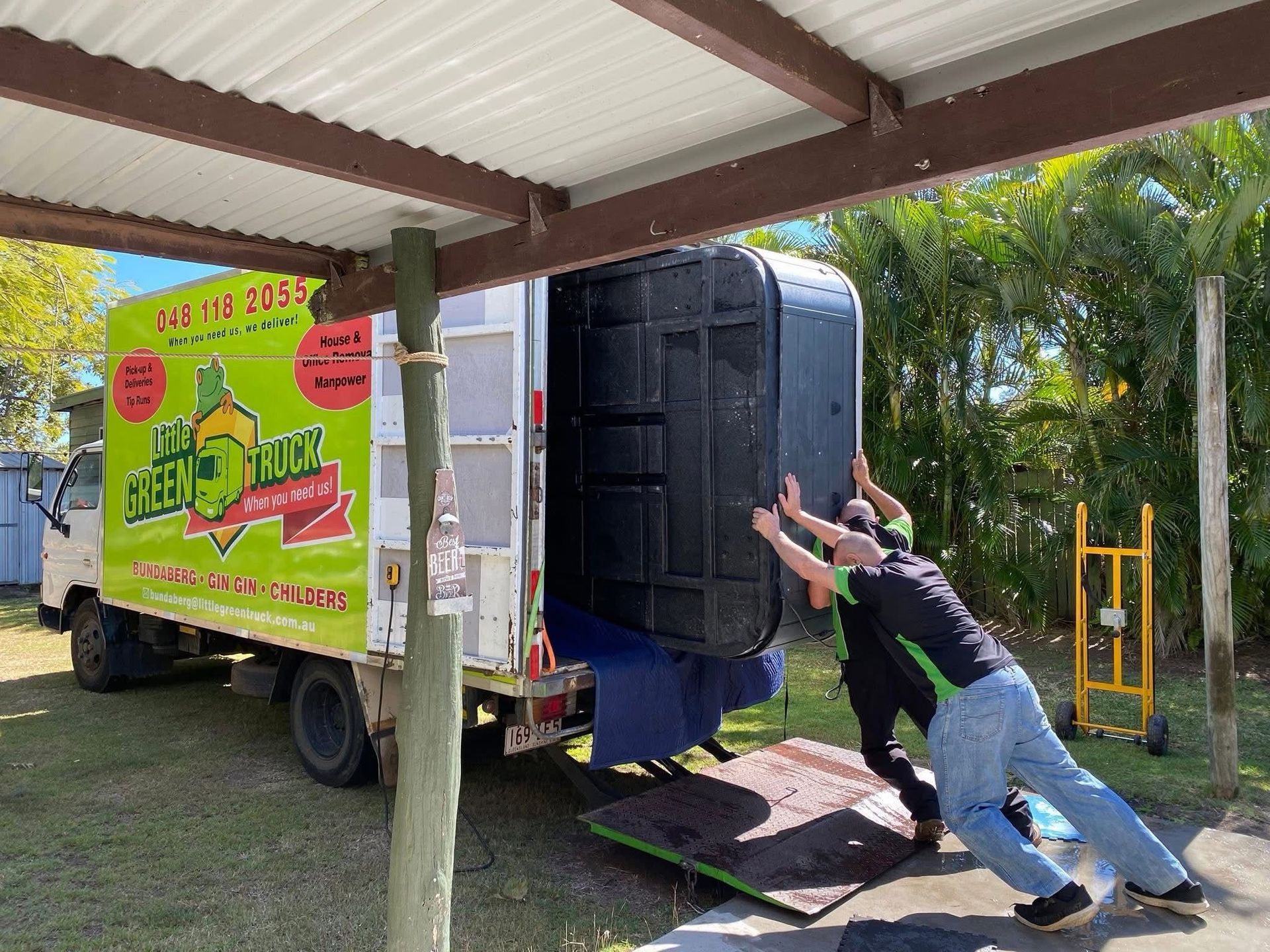 Man Pushing a Black Appliance up A Ramp Into a Bright Green Moving Truck Under a Carport — Little Green Truck Bundaberg in Bargara, QLD