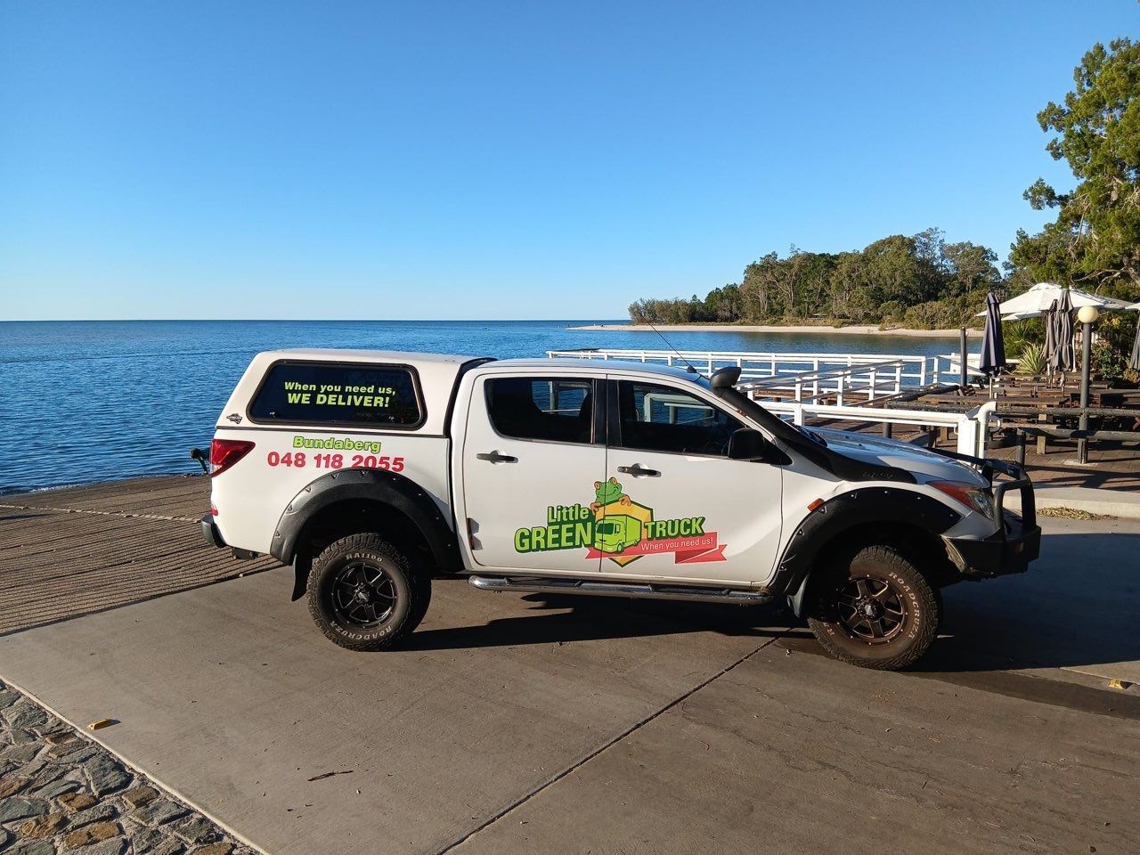 White pickup truck with company graphics parked by a waterfront promenade on a sunny day