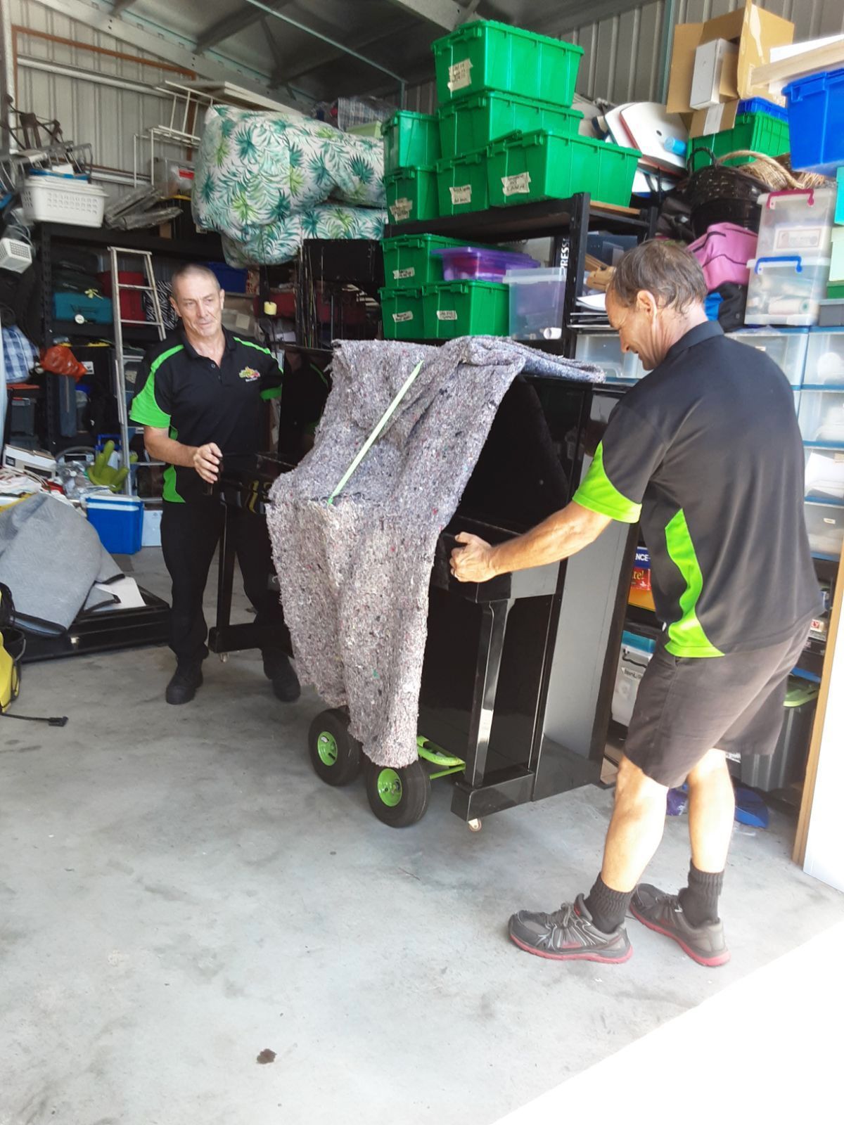 Two Workers Move a Large Wrapped Item on a Wheeled Cart — Little Green Truck Bundaberg In Gladstone, QLD