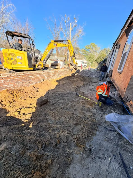 Construction site with excavator and bulldozer beside a brick building, worker in orange vest on muddy ground