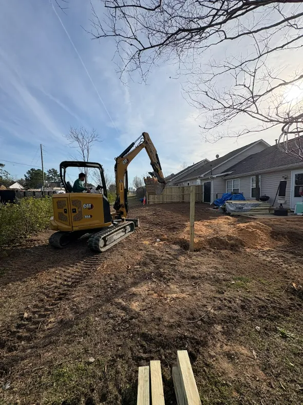 Backhoe excavating a yard beside a row of houses under a clear sky