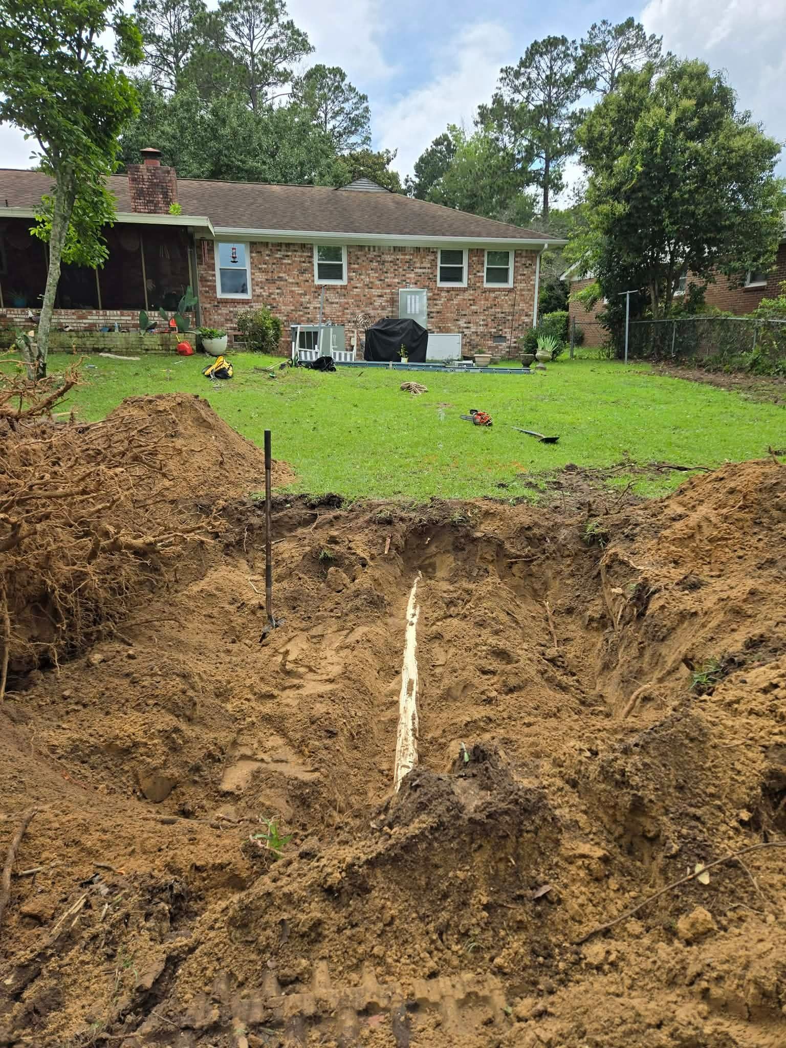 Backyard with a large muddy sinkhole in the foreground and a brick house in the background