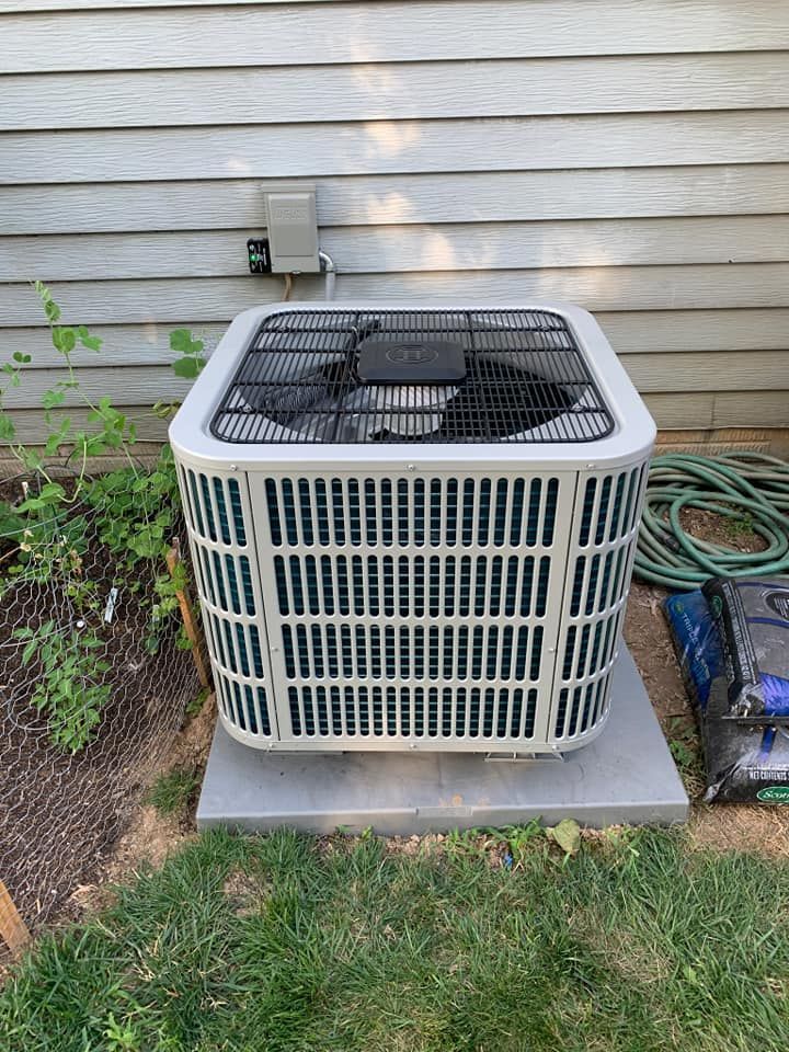 An air conditioner is sitting outside of a house next to a hose.