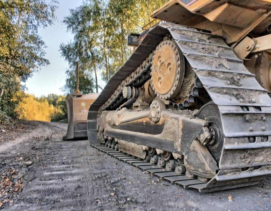 Close-up of a yellow bulldozer track on a dirt road with trees in the background