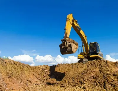 Yellow excavator lifting dirt on a construction site under a blue sky