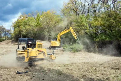 Yellow excavator and loader working on a dusty clearing near trees