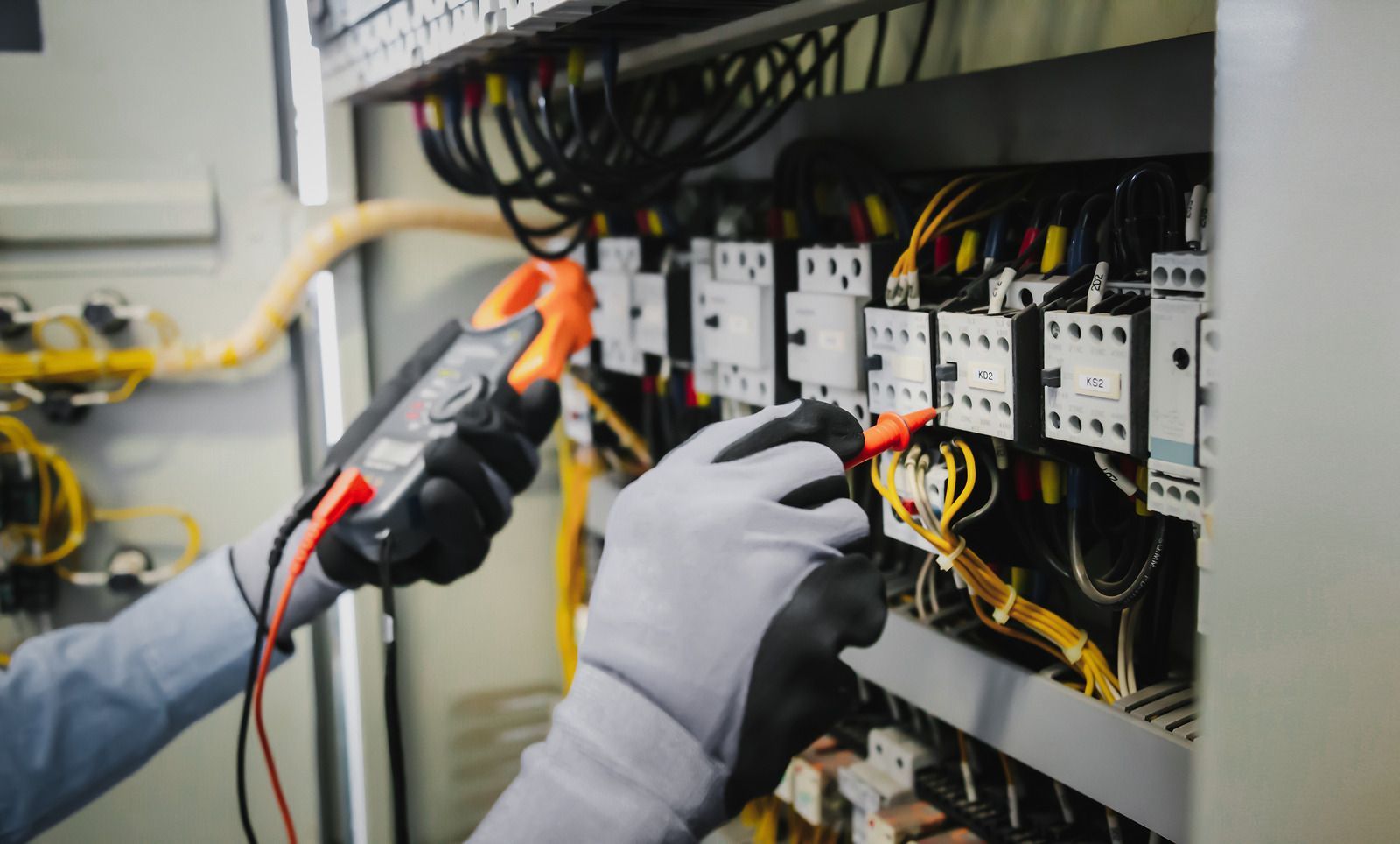 An electrician is working on an electrical box with a multimeter.
