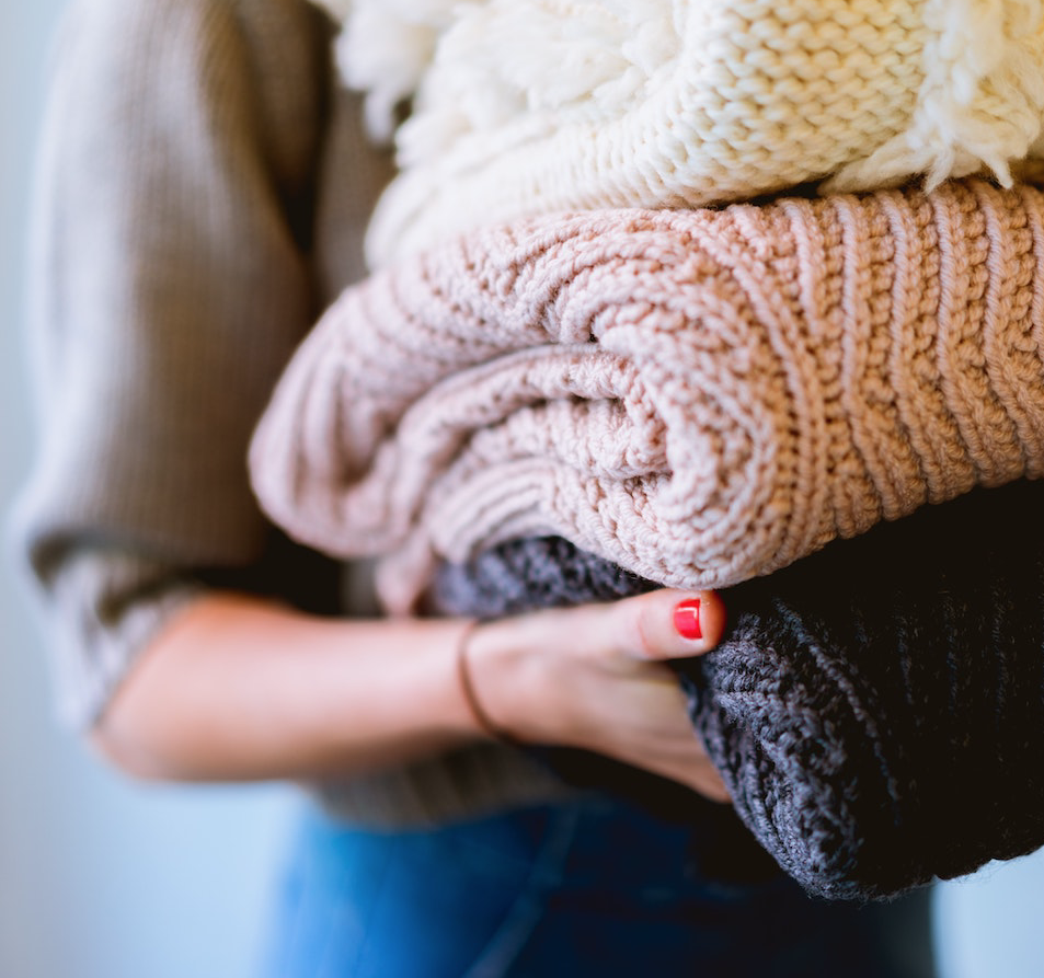 A woman is holding a pile of sweaters in her hands.