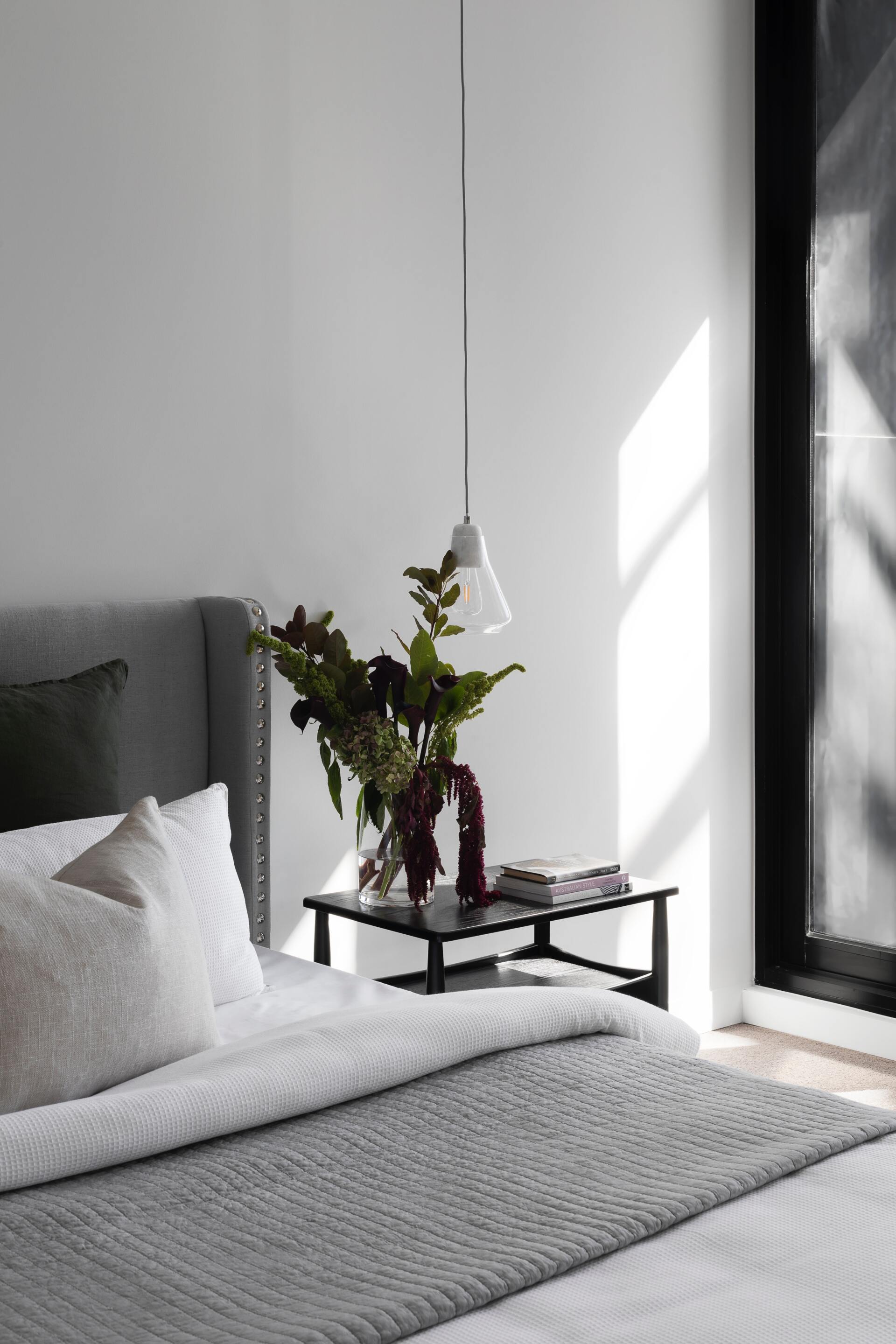 A bedroom with a bed and a nightstand with a vase of flowers on it.