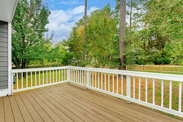 An empty deck with a white railing and trees in the background.