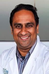 A man in a white coat and tie is smiling for the camera