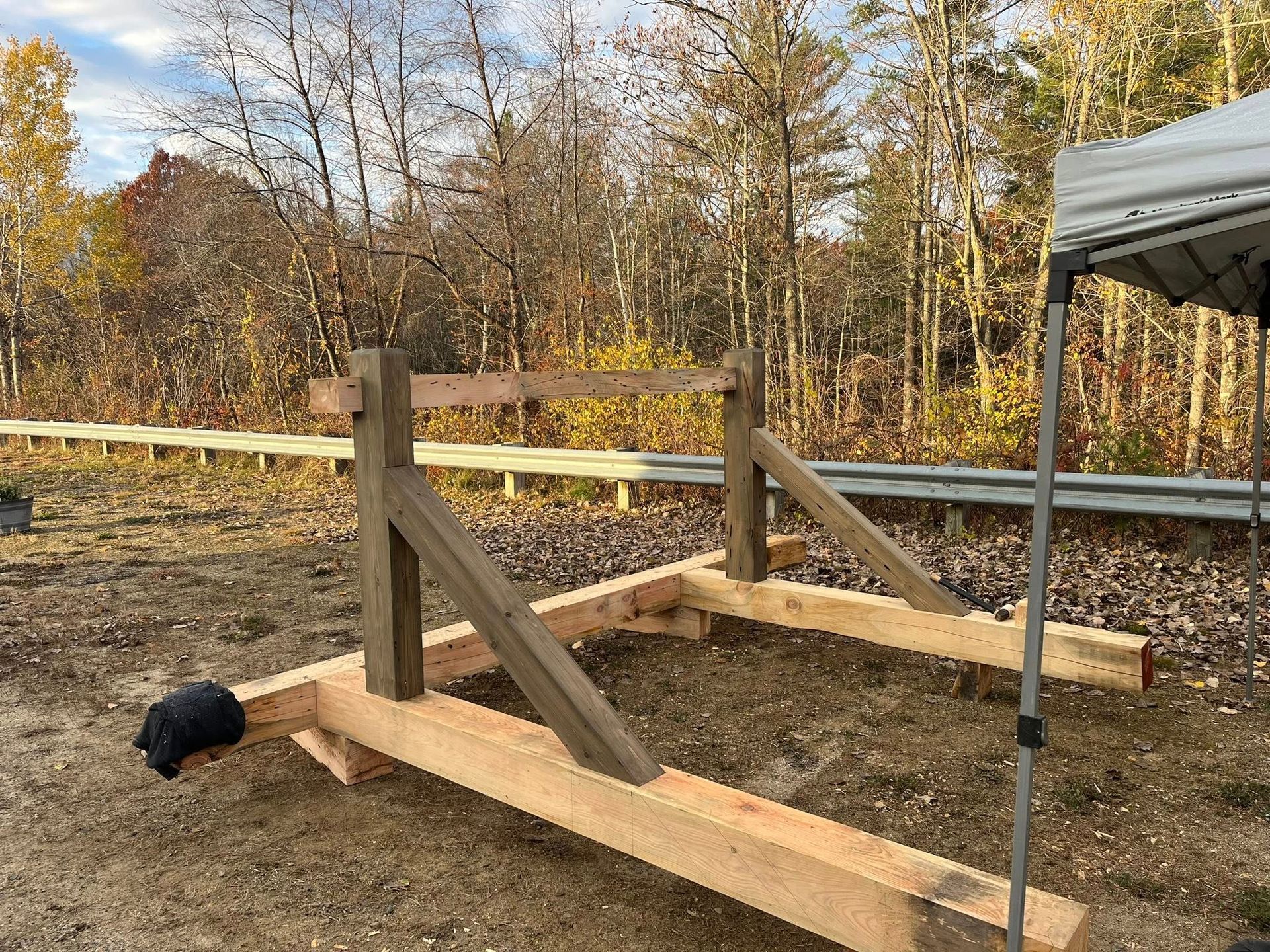 A wooden timber frame structure rests on the ground outdoors, featuring two vertical posts braced by diagonal supports.
