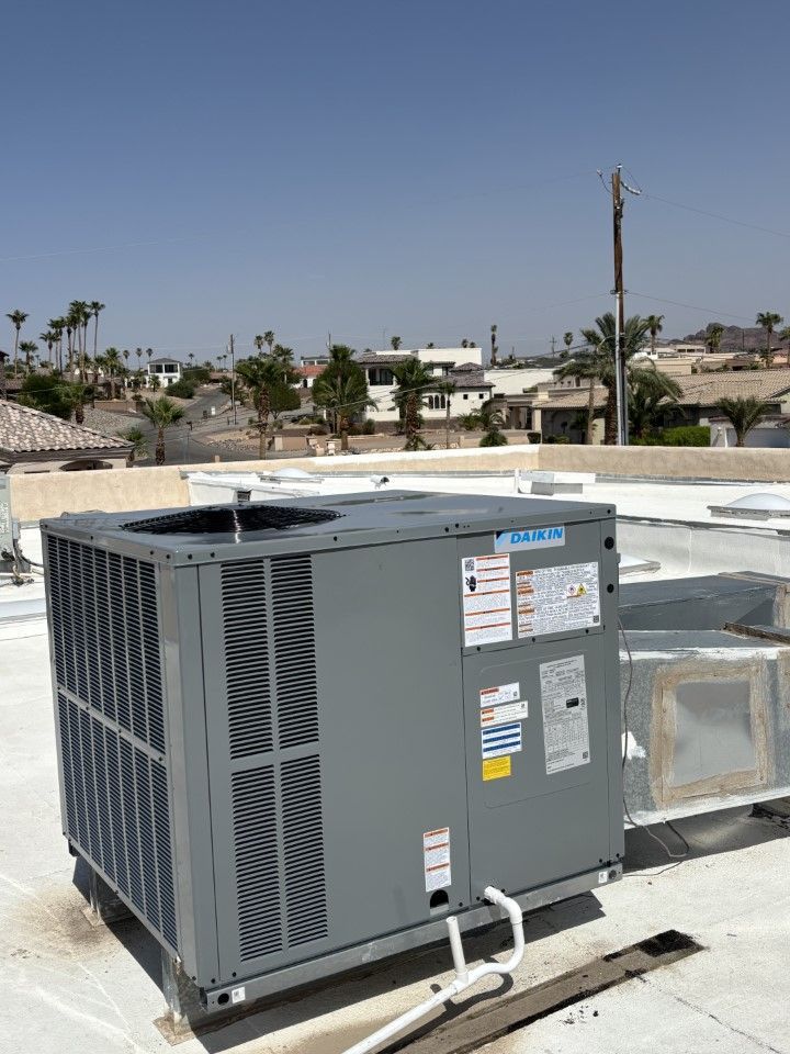Gray Carrier air conditioning unit on a white rooftop, with buildings and clear sky in the background.