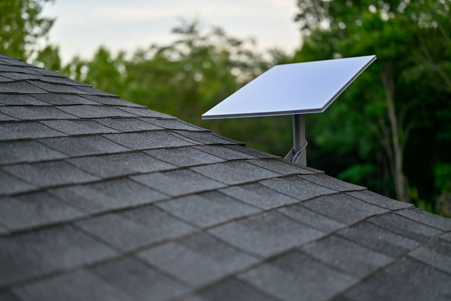 Solar panel mounted on a shingled roof with trees in the background