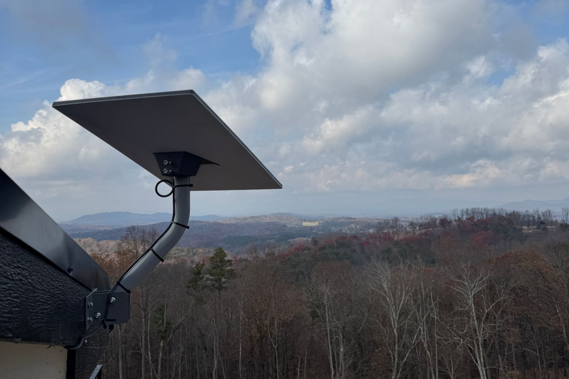 Solar panel mounted on a pole overlooking a cloudy forested hillside and distant landscape