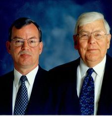 Two men in suits posing against a blue studio backdrop