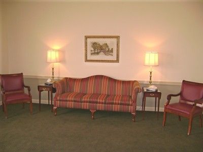 A cozy sitting room with a striped sofa, two chairs, lamps, and a framed picture on a cream wall.