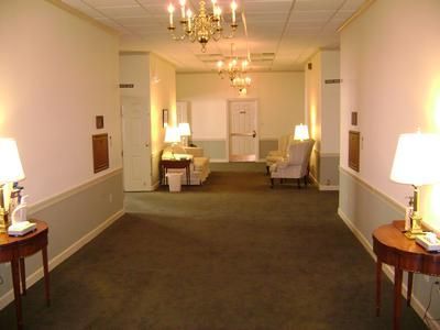 Long hotel hallway with chandeliers, lamps, chairs, and a carpeted floor