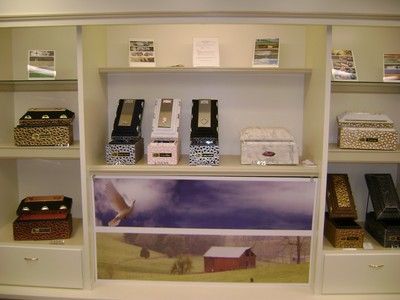 White display shelves holding small decorative boxes and framed photos above a landscape mural.