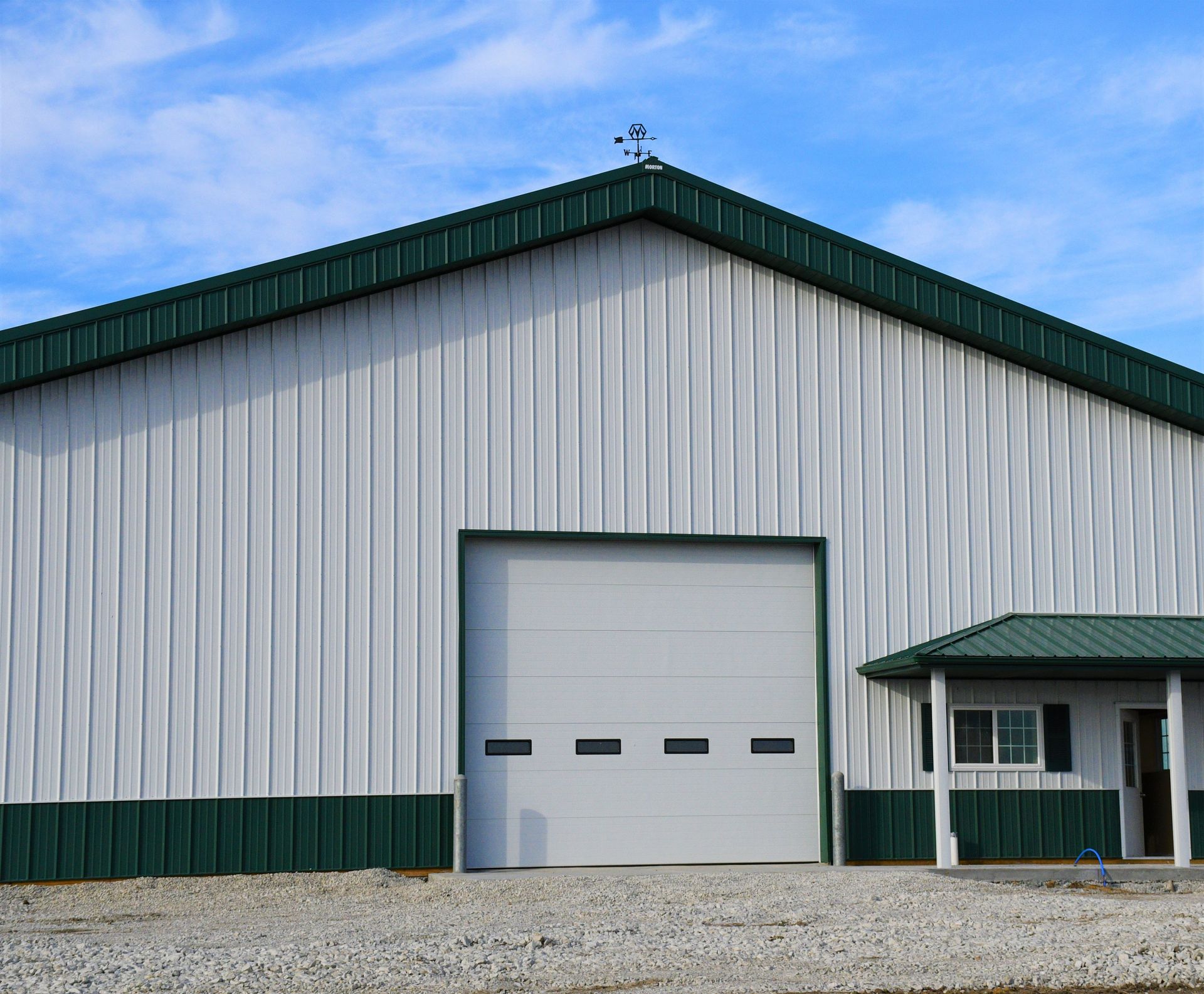 Large white metal building with green trim and a large garage door. Small adjacent building.