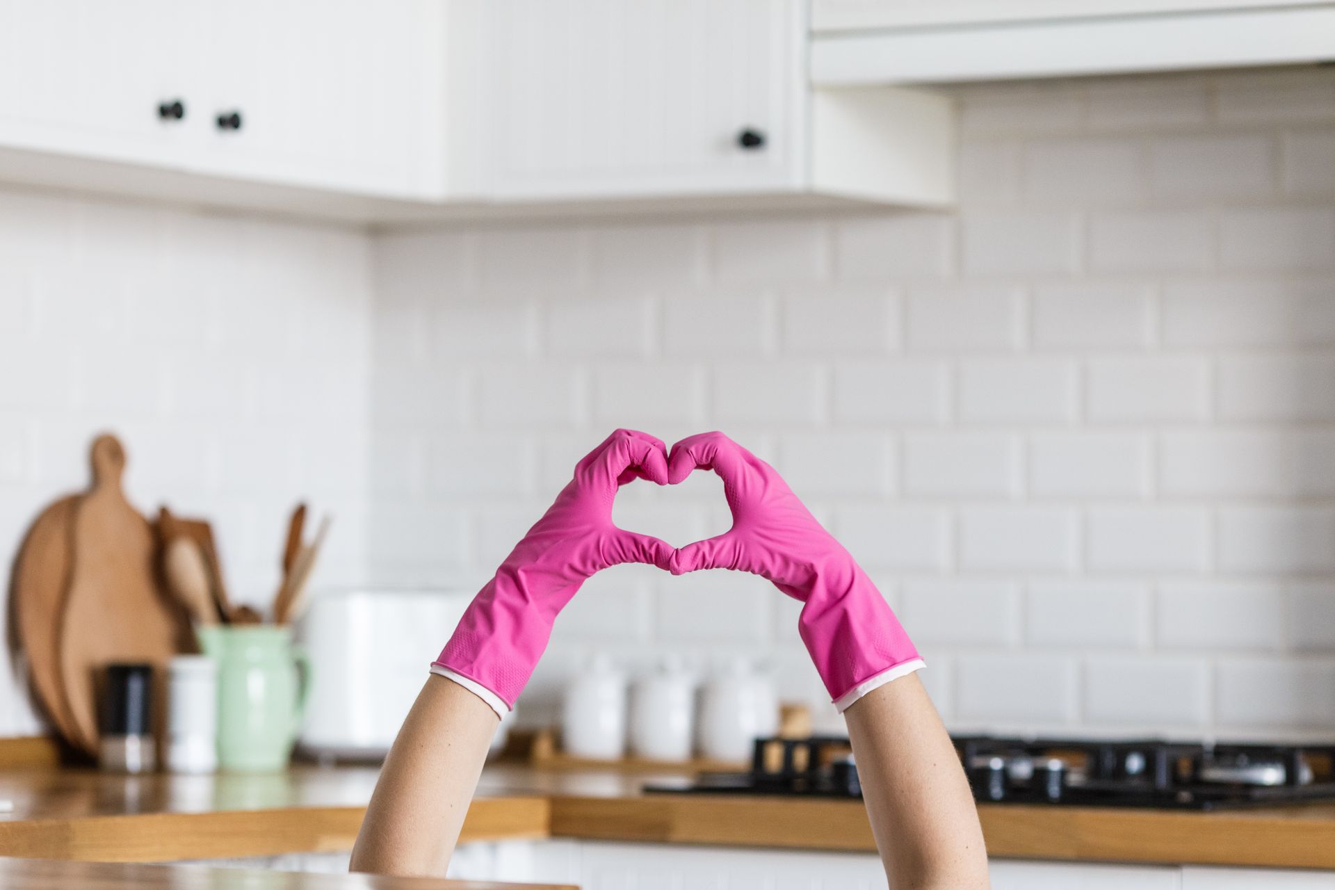Hands in pink gloves forming a heart in a white kitchen.