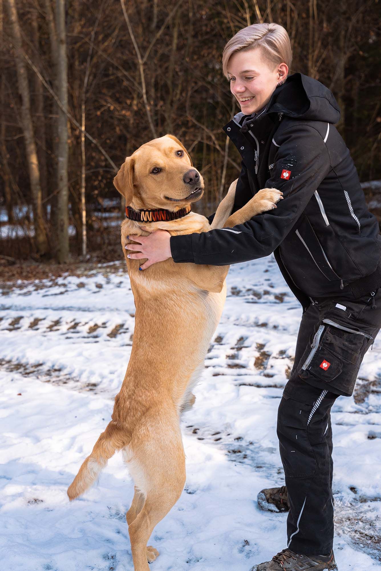 Ein Mädchen hält einen Hund im Schnee auf seinen Hinterbeinen.