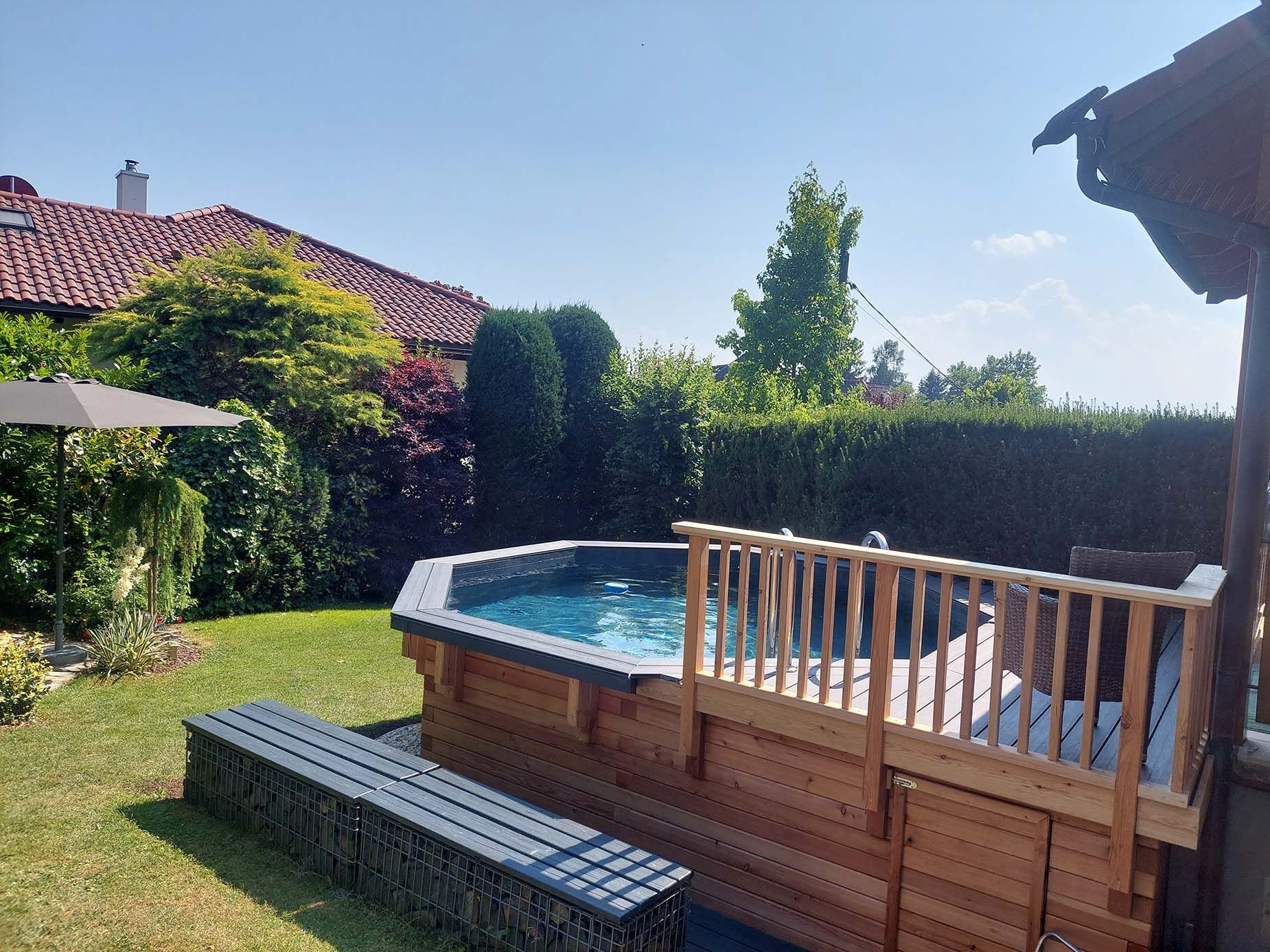 Aufstellpool mit Holzdeck und Geländer in einem sonnigen Hinterhof.