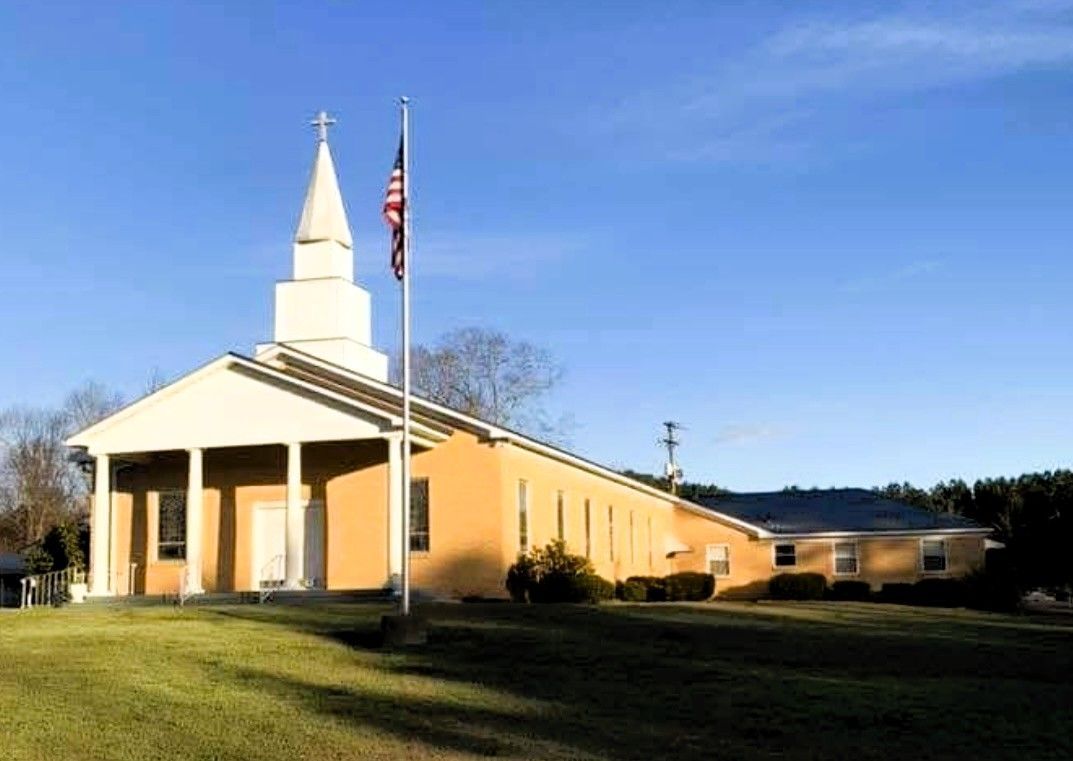 Small white church with steeple and U.S. flag in a grassy field under a blue sky