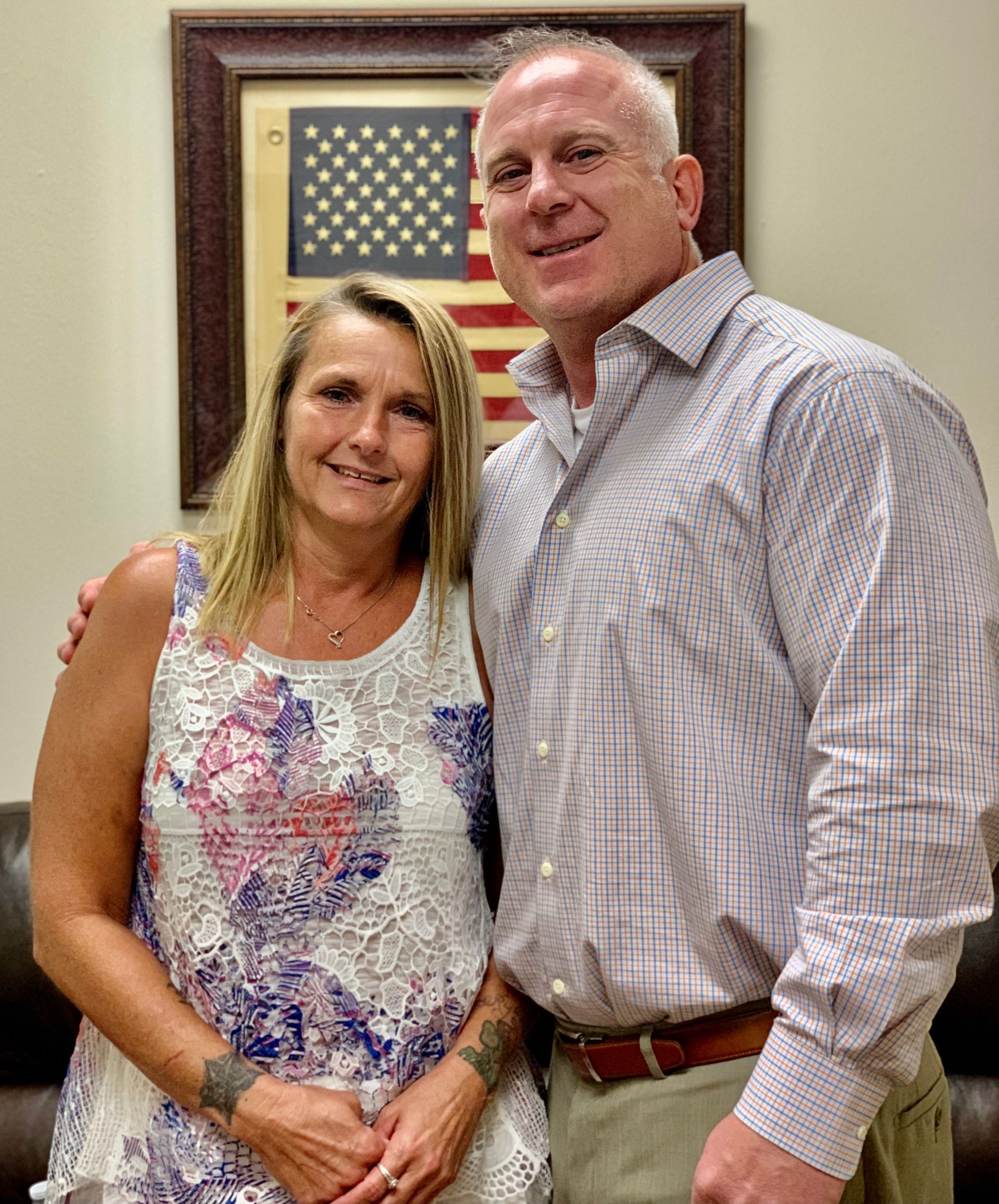 A man and a woman are posing for a picture in front of an american flag.