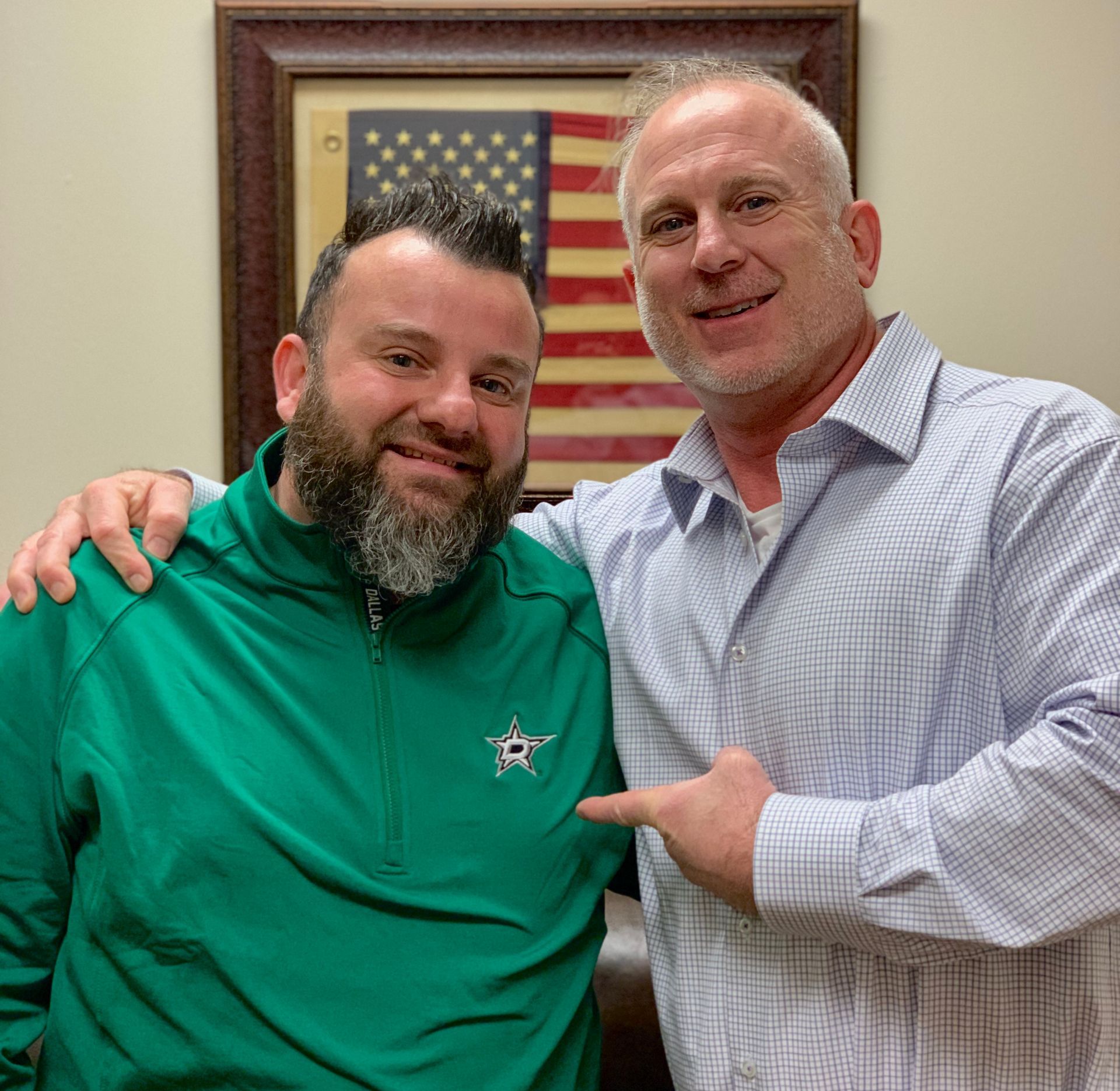Two men are posing for a picture in front of an american flag.