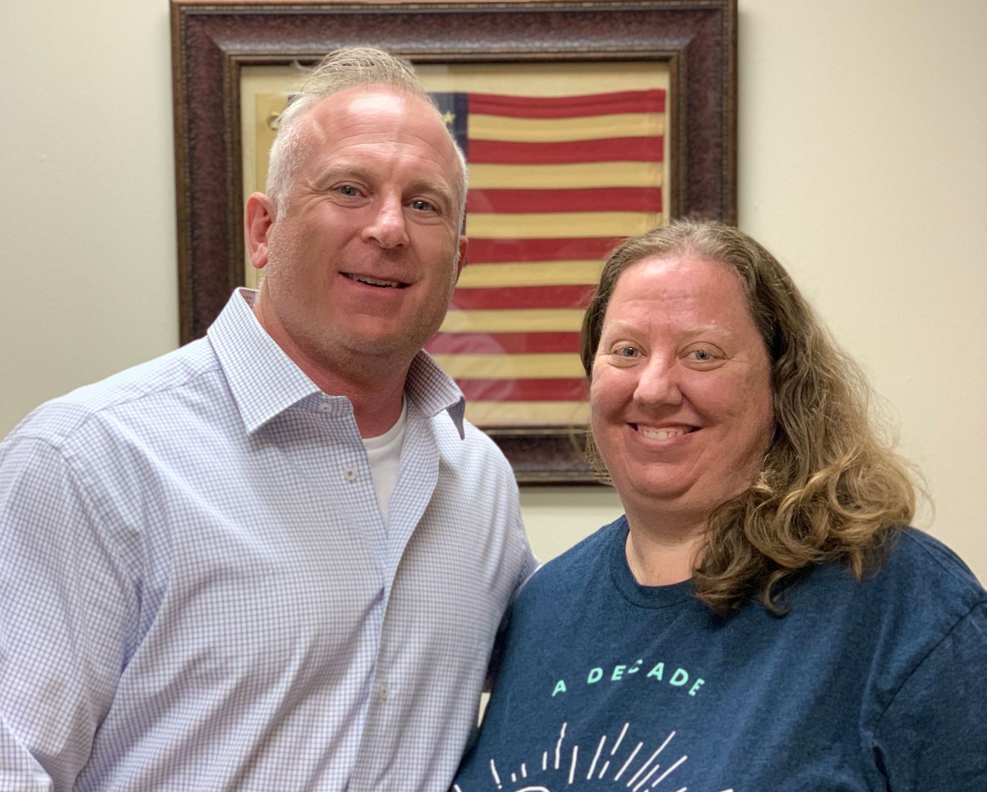 A man and a woman are posing for a picture in front of an american flag.