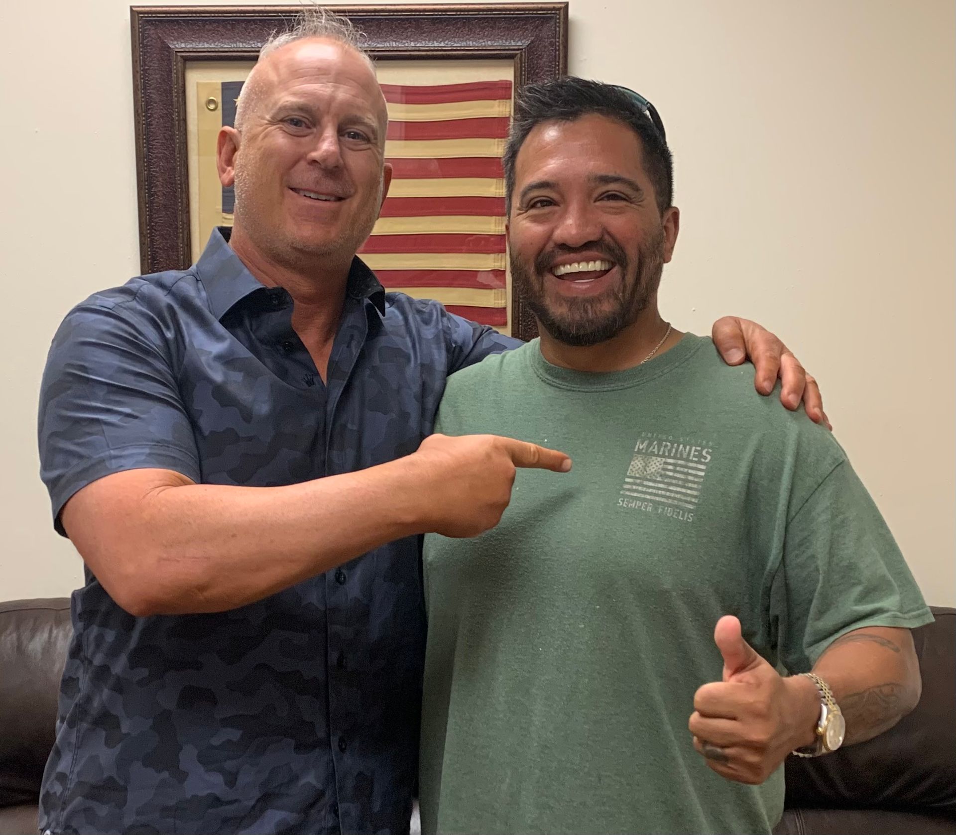 Two men are posing for a picture in front of an american flag.