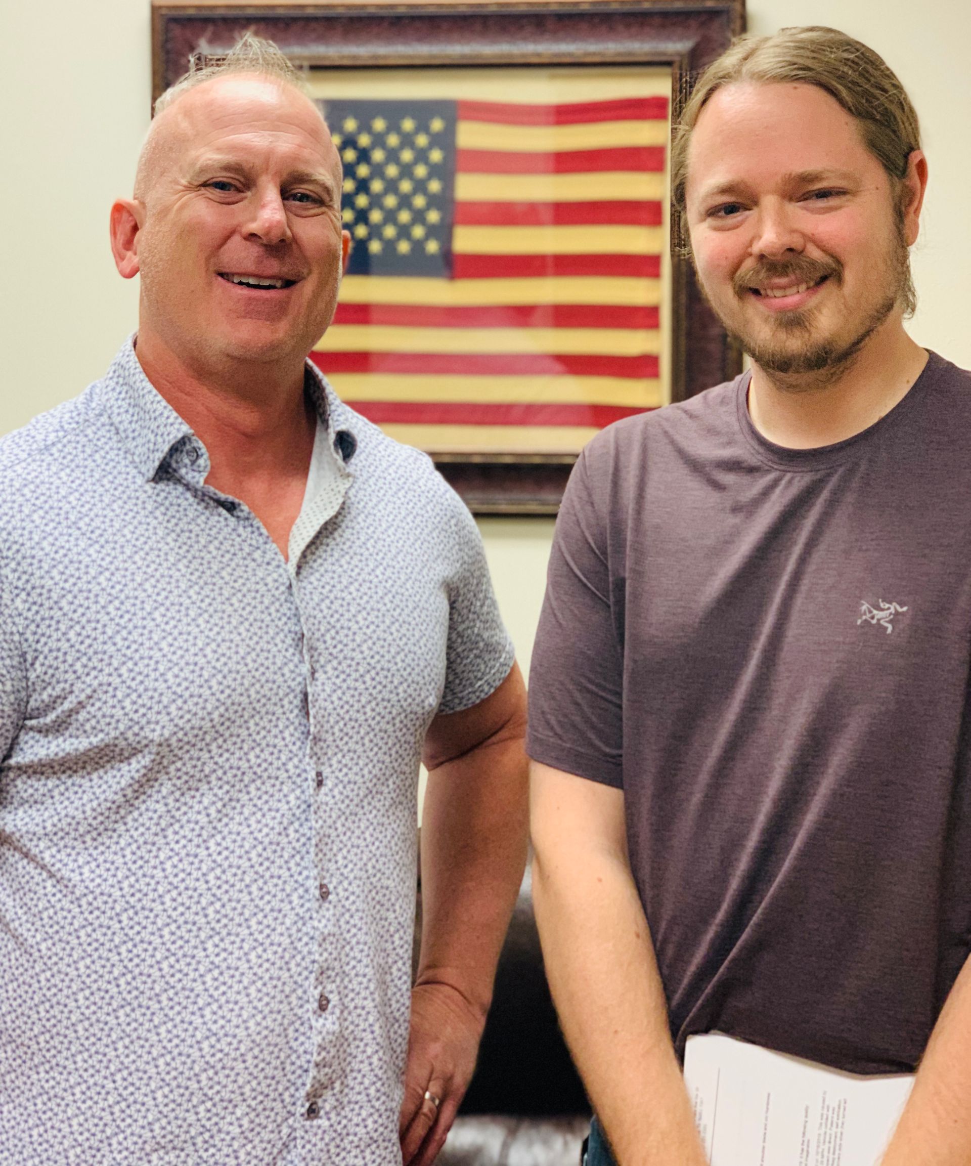 Two men are posing for a picture in front of an american flag