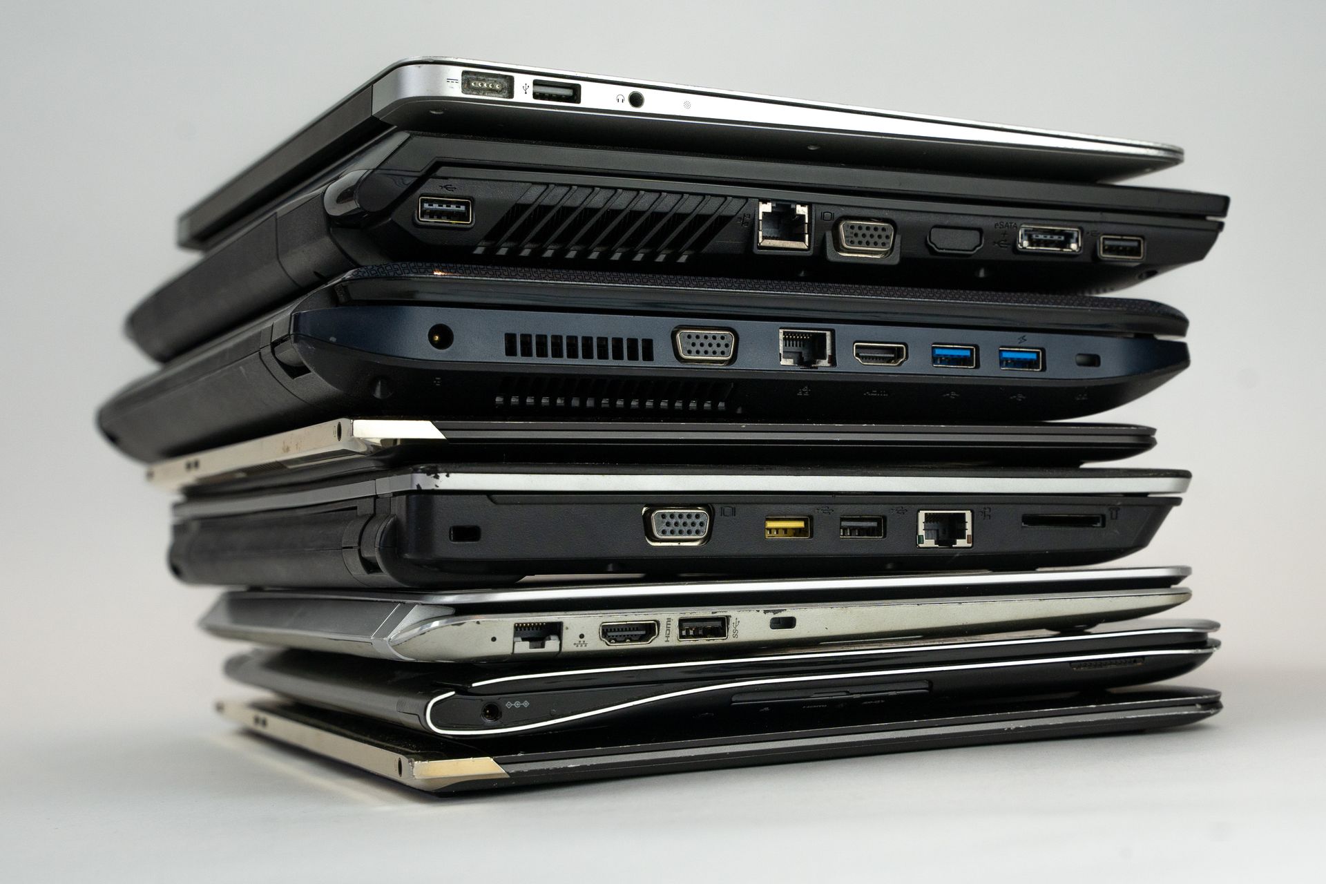 A stack of closed laptops viewed from the side showing USB, HDMI, and Ethernet ports