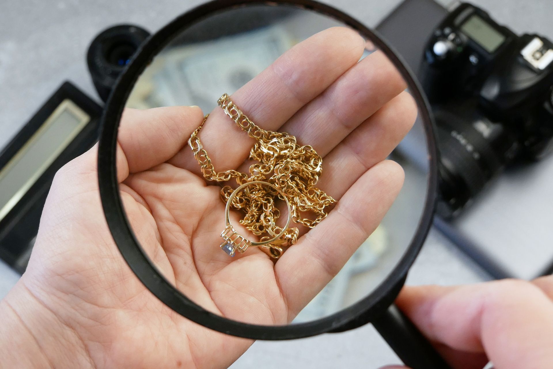 Magnifying glass examining gold jewelry resting in an open hand. Magnifying glass examining gold jewelry resting in an open hand.