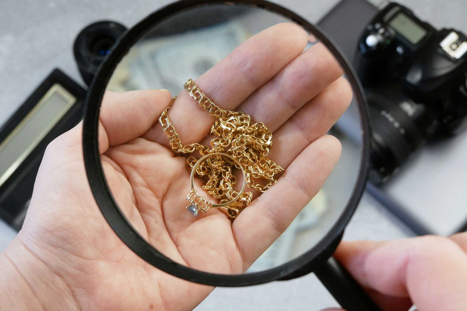 Magnifying glass inspecting gold jewelry held in an open hand.