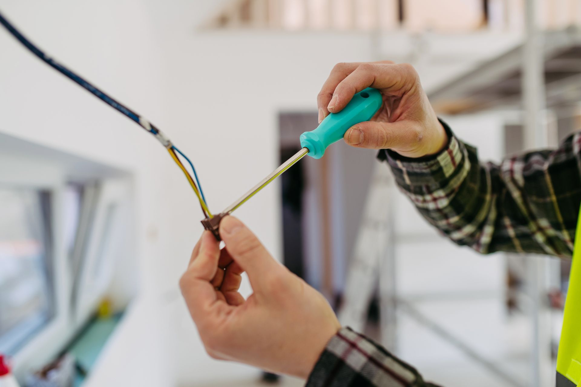 Electrician using a screwdriver to connect wires, indoors, with safety vest and plaid shirt. Electrician using a screwdriver to connect wires, indoors, with safety vest and plaid shirt.