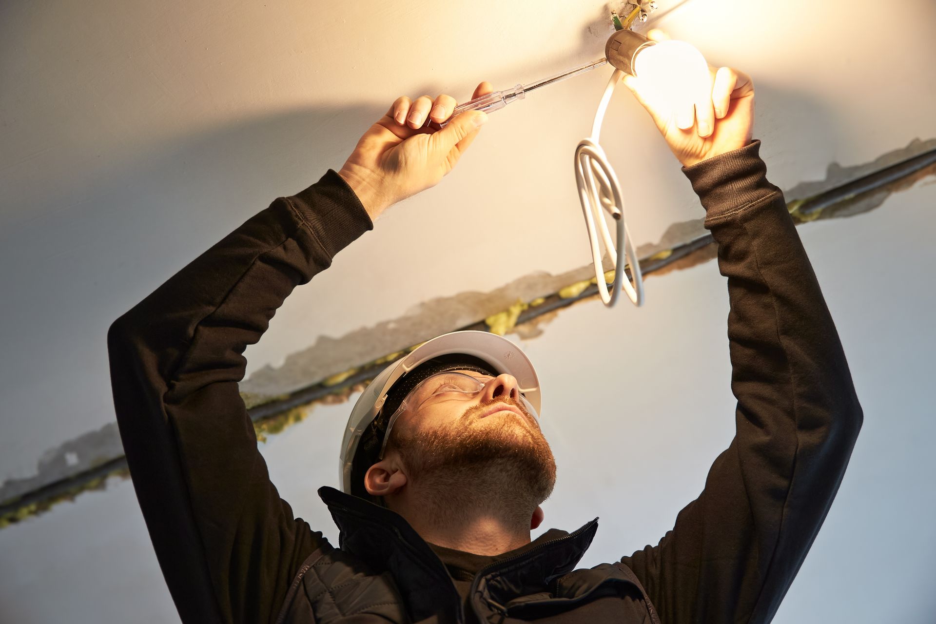 Electrician installing ceiling light fixture and wiring during electrical repair work.