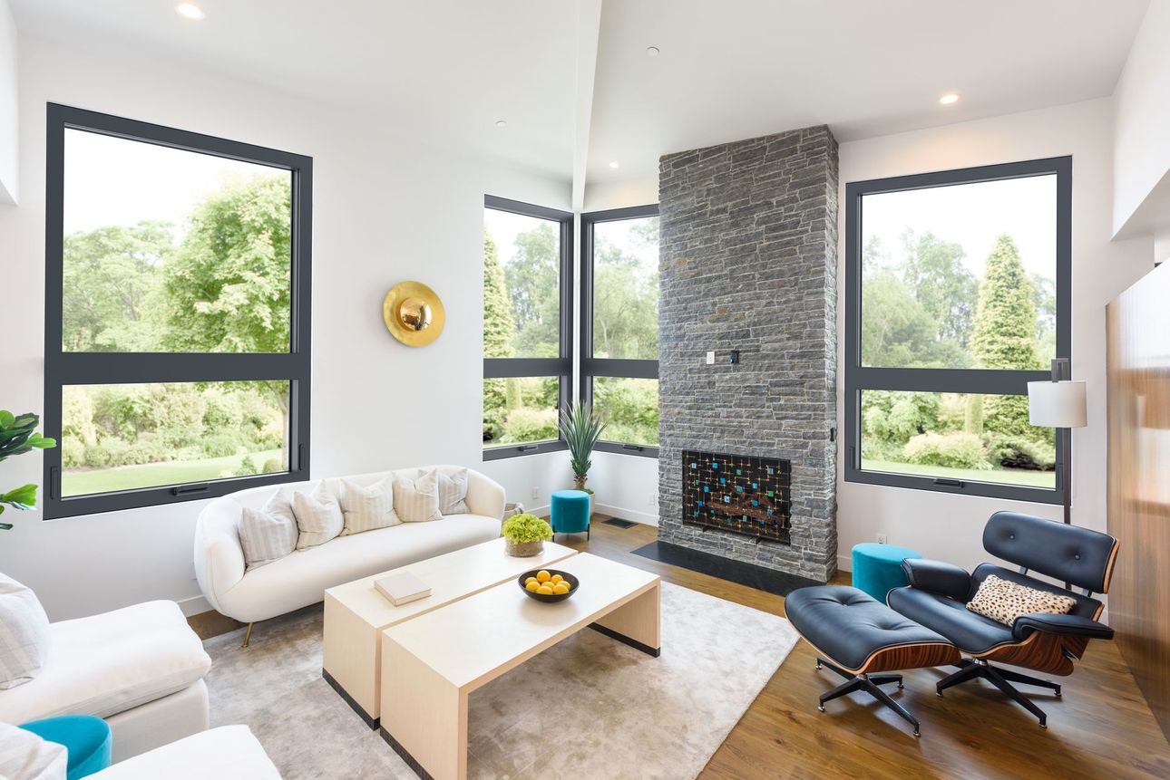 Modern living room with white sofas, blue chair, large windows, and stone fireplace.