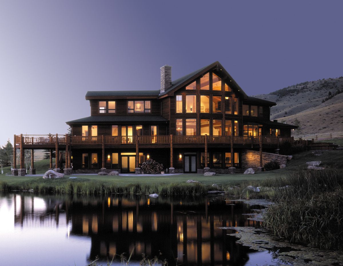 Lit mountain lodge with warm windows reflected in a calm lake at dusk