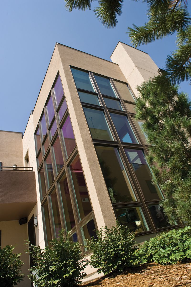 Modern building exterior with tall glass windows and beige walls, viewed from below with trees in the foreground