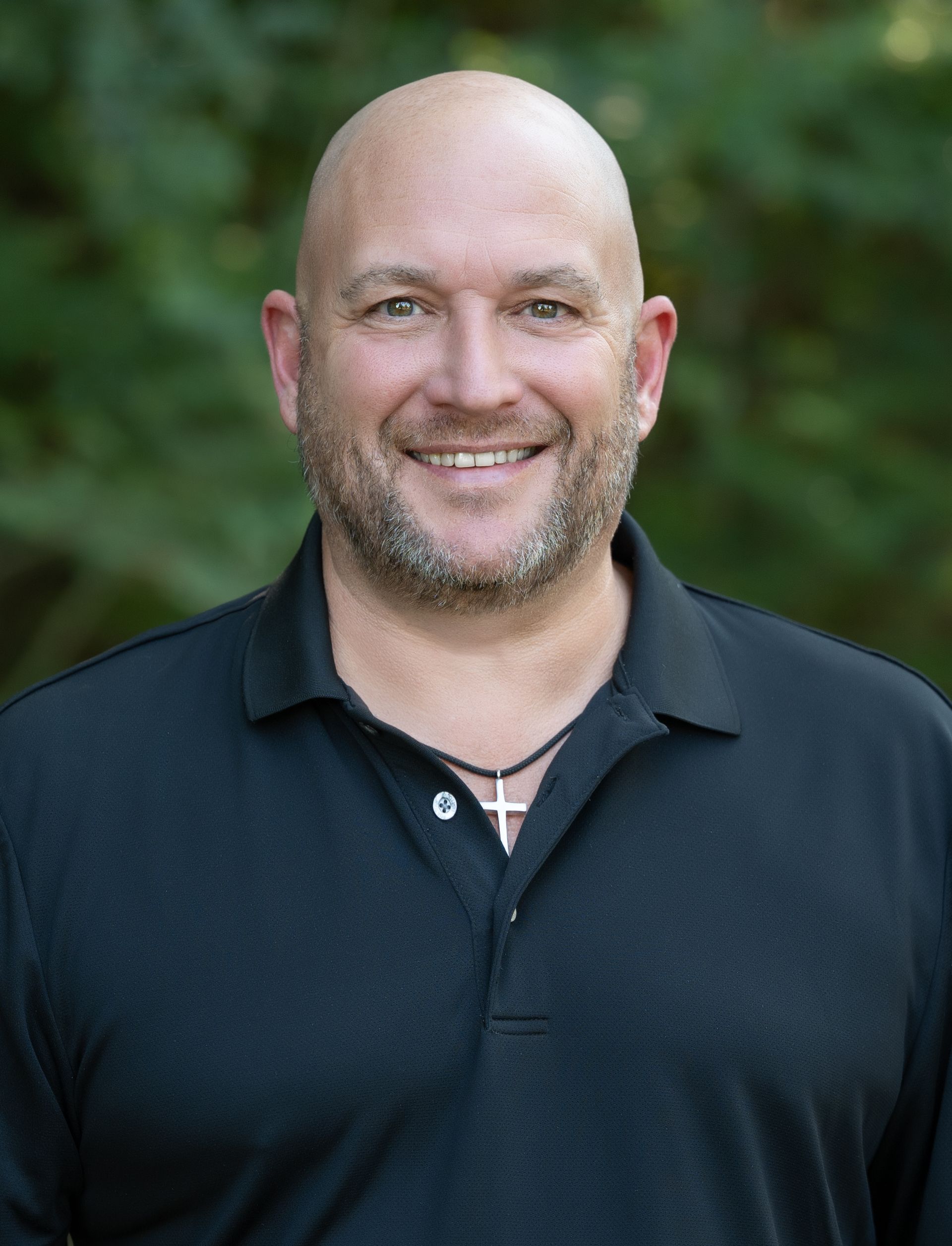 A bald man with a beard is wearing a black shirt and a cross necklace.