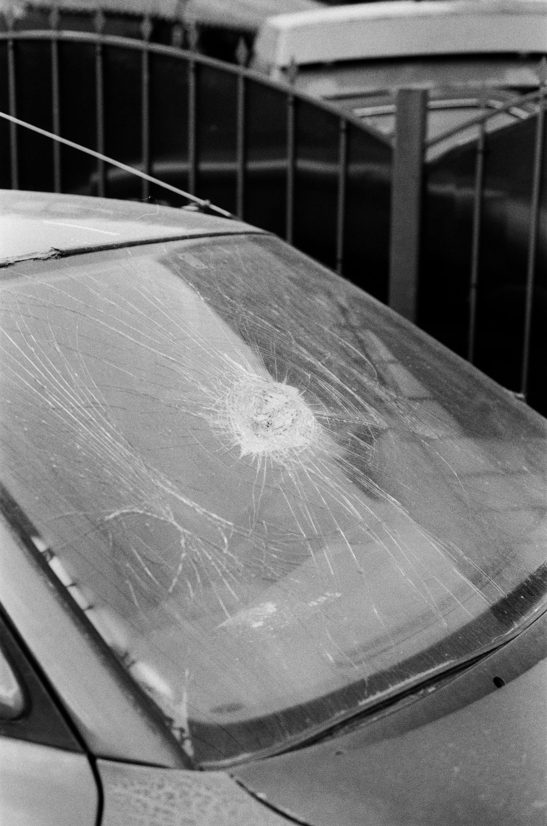 Frost-covered car windshield with ice and snow buildup parked near a fence.