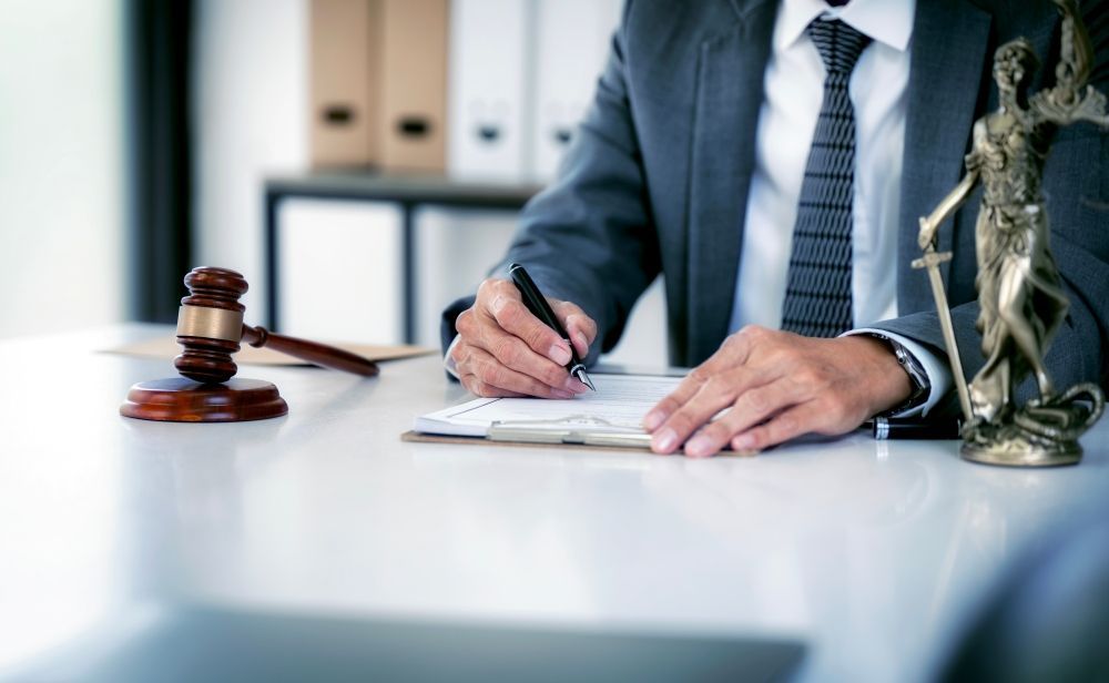 A Man In A Suit And Tie Is Sitting At A Desk With A Statue Of Justice — O'Reilly & Sochacki Lawyers in Gold Coast, NSW
