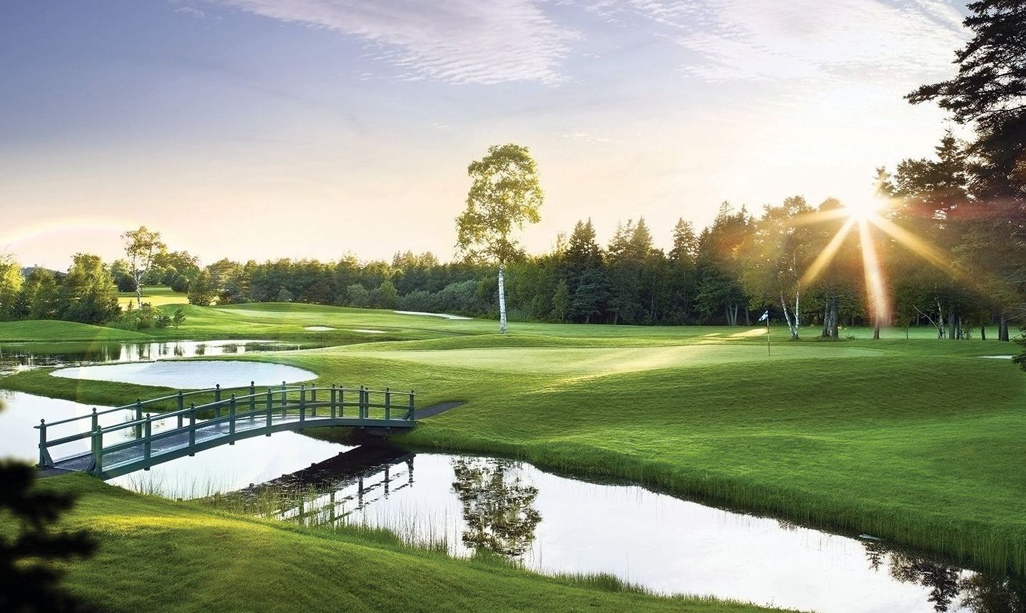A bridge over a pond on a golf course with the sun shining through the trees