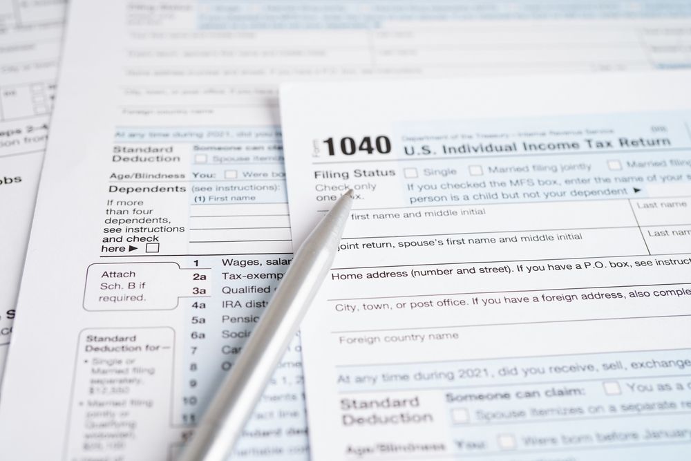 A pen rests on a 1040 U.S. Individual Income Tax Return form, documents visible in the background.